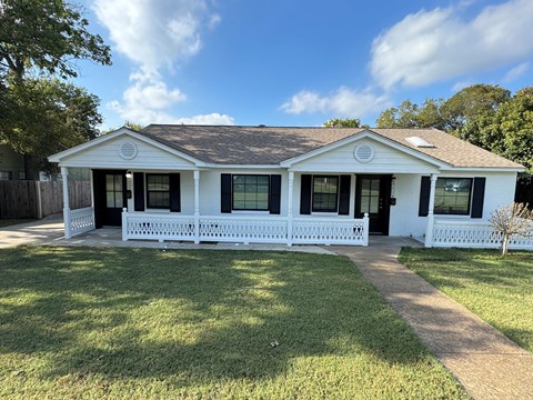 A white house with a brown roof and a white fence.